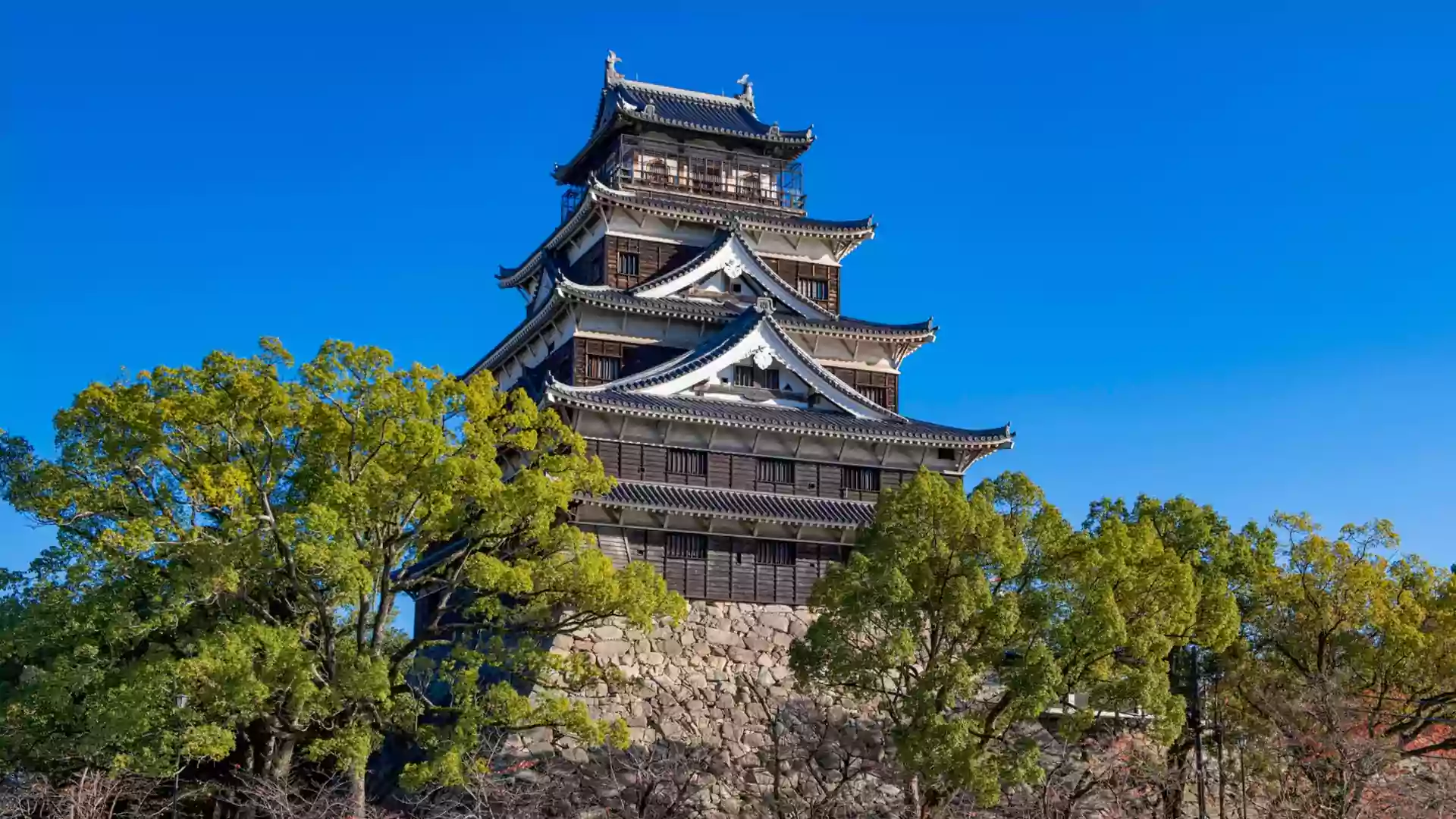 Hiroshima Castle Jepang dengan arsitektur tradisional megah, dikelilingi pepohonan hijau dan langit biru cerah.