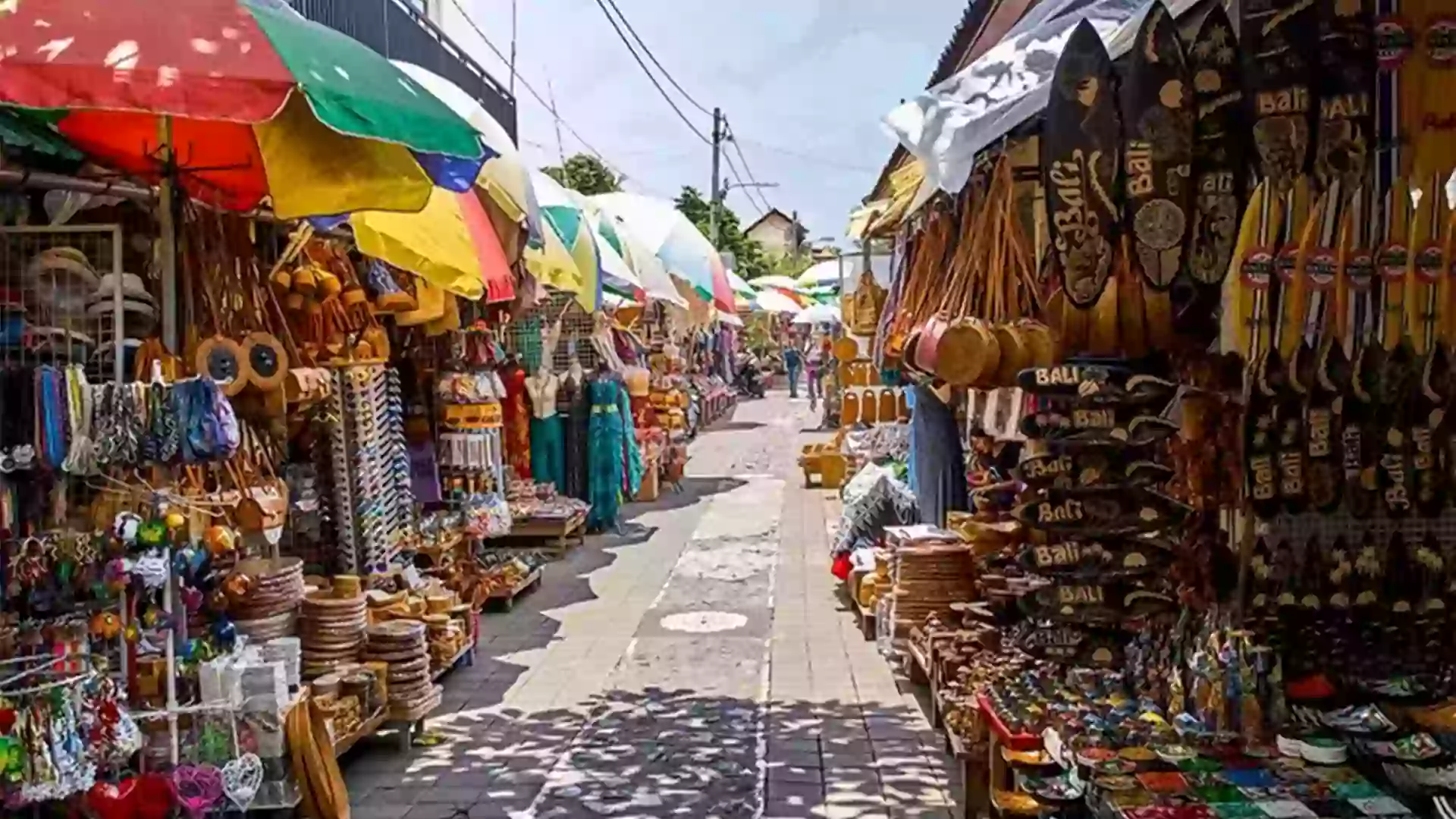 Suasana Pasar Seni Kuta yang penuh warna dengan deretan Souvenir Bali, tas rotan, dan kerajinan tangan lokal.