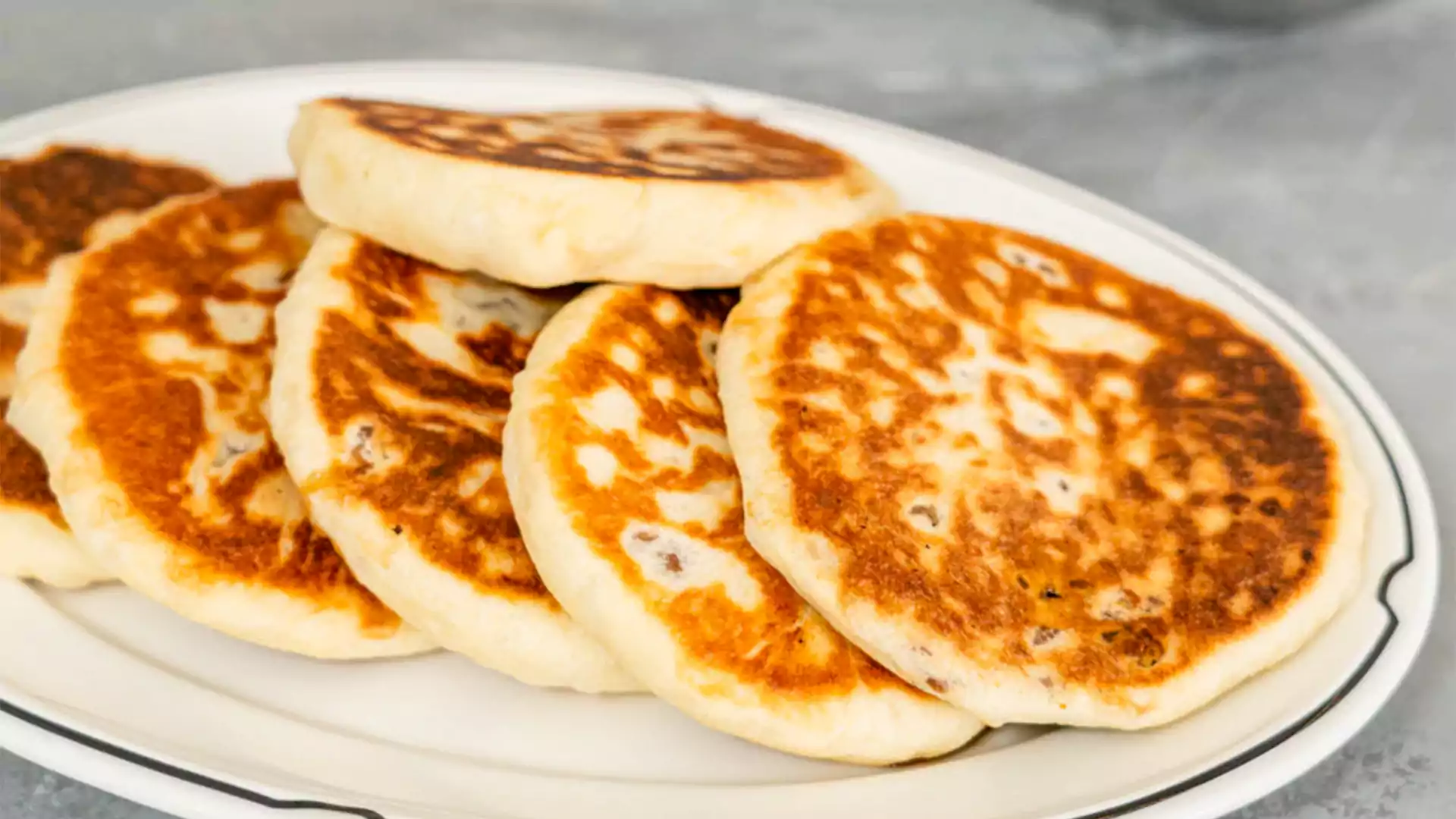 Beberapa buah hotteok atau pancake manis khas Korea dengan kulit kecokelatan renyah, tersaji di atas piring putih siap santap.