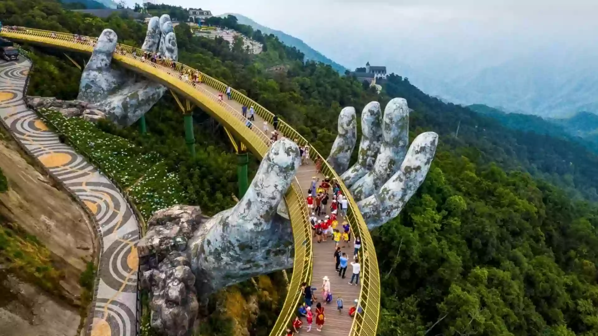 Golden Bridge di Da Nang, Vietnam, dengan jembatan emas yang ditopang patung tangan raksasa di atas perbukitan hijau dan kabut pegunungan.