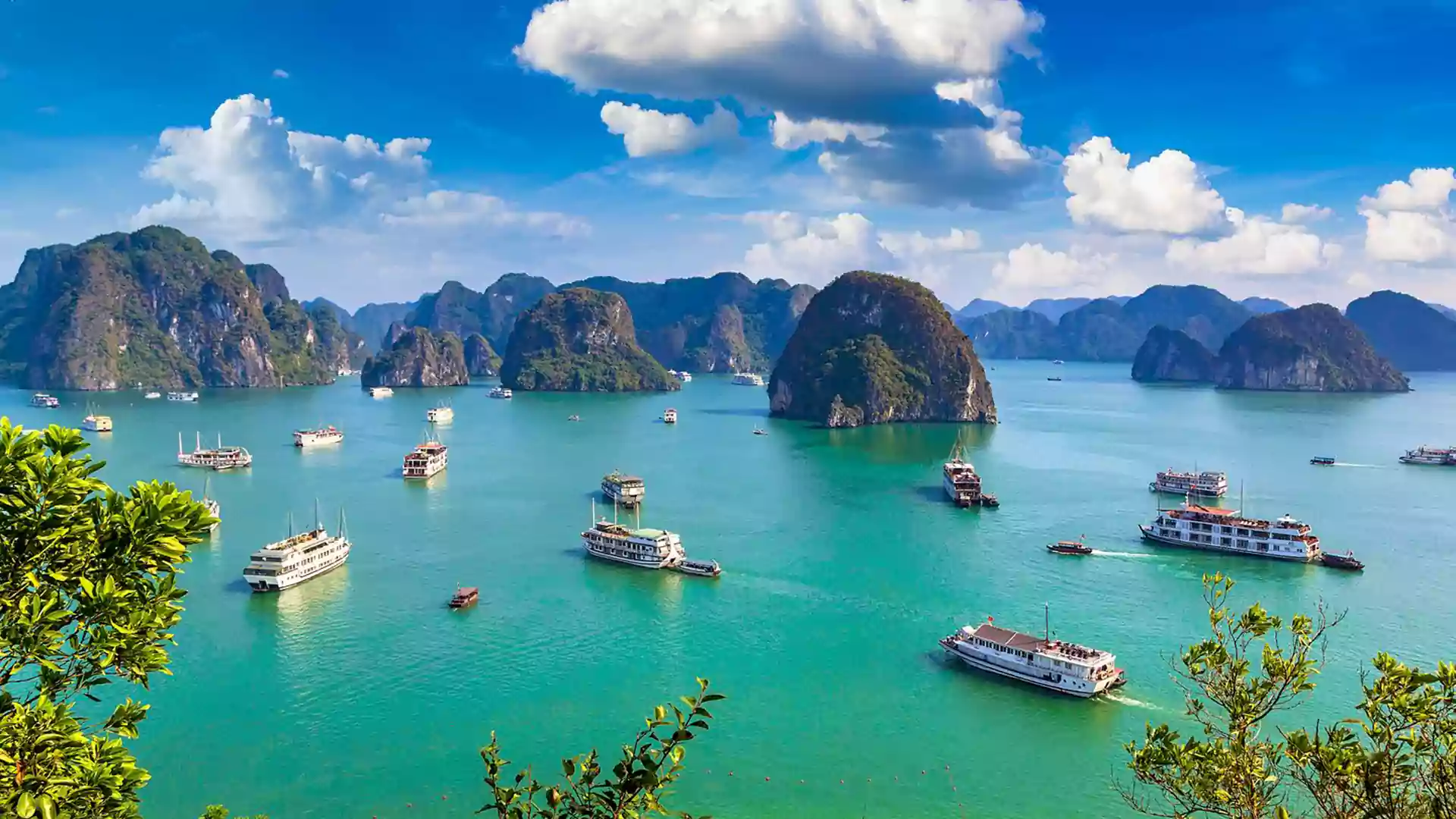 Pemandangan Ha Long Bay di Vietnam dengan air laut hijau kebiruan, kapal wisata putih, dan gugusan pulau batu kapur di bawah langit cerah.