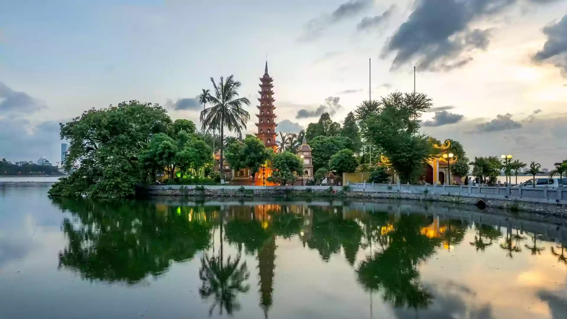 Danau di Hanoi dengan pagoda tradisional Vietnam dan pepohonan hijau yang memantulkan bayangan di air saat senja