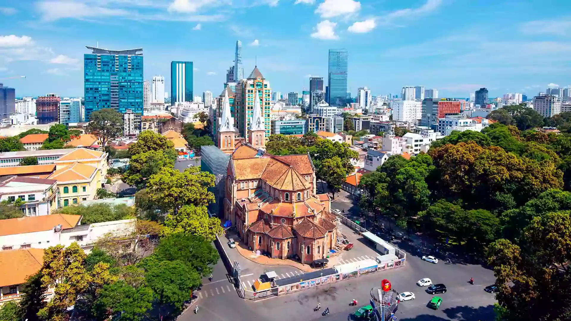 Pemandangan udara Ho Chi Minh City dengan Katedral Notre-Dame Saigon, jalan raya kota, pepohonan hijau, dan gedung-gedung modern di sekitarnya.