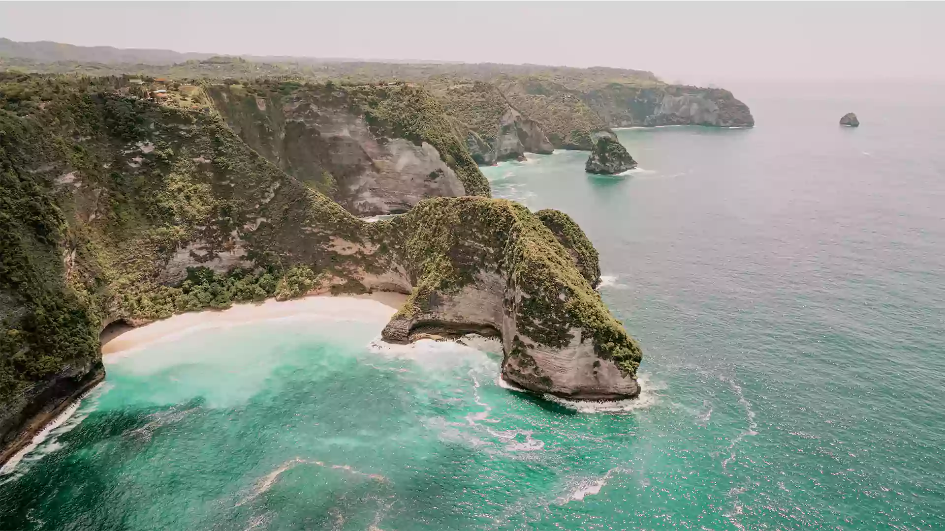 Tebing karang Nusa Penida Bali dengan pantai tersembunyi, air laut turquoise, dan ombak yang menghantam tebing.